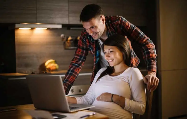 An expecting couple on looking at a computer.